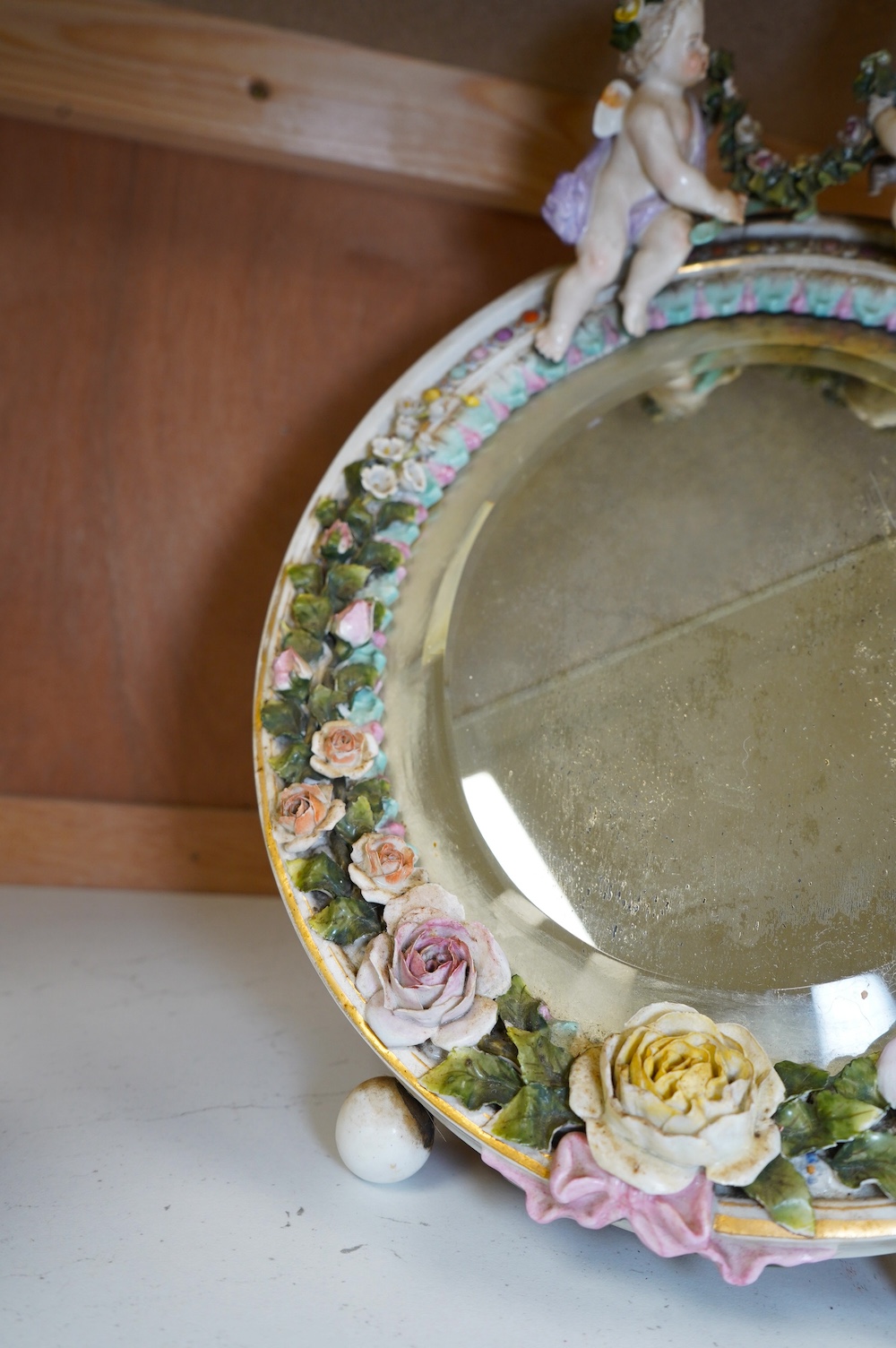 A Sitzendorf easel framed mirror, mounted with two putti holding a swag of roses, 35cm high. Condition - some damage to roses